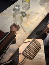 Cartera de mano tipo clutch, de cuero trenzado a mano en color negro y beige, con diseño de rayas verticales.