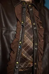 Campera de cuero color marrón con cuello clásico, cierre frontal con botones metálicos y detalles de volados en gamuza a lo largo de la botonadura y en los puños.