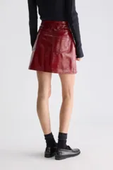 Minifalda evasé de tiro alto, confeccionada en material sintético de acabado brillante, estilo charol, con diseño de cinco bolsillos y cierre frontal con botón y cremallera.