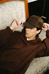 Gorra trucker marrón con frente de tela y parte trasera de rejilla. Presenta un bordado 3D con un diseño abstracto en el frente.