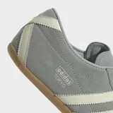 Championes Adidas modelo Tokyo, de diseño retro y corte bajo. Confeccionados en gamuza color verde grisáceo con las icónicas tres tiras laterales en color crema y suela de caucho color caramelo.