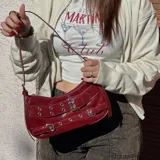 Cartera tipo baguette color bordó charol, con correa corta ajustable y detalles de hebillas y ojalillos metálicos.