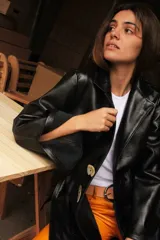 Blazer de cuero color celeste metalizado, con solapas, cierre con broches tipo tanca de madera y puños con detalle de piel sintética marrón.