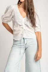 Blusa marrón de algodón con bordados sutiles, escote en V, mangas cortas abullonadas y detalle de fruncido con cordón ajustable en el centro del frente.