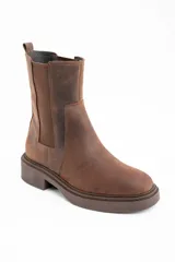Bota tipo Chelsea de caña media, confeccionada en cuero legítimo color marrón con acabado mate. Presenta paneles laterales elásticos al tono y una suela de goma robusta con plataforma baja.
