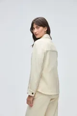 Camisa de lana fina sin teñir, color marrón, con diseño capitoneado y pespuntes decorativos. Presenta cuello clásico, cierre frontal con botones metálicos y dos bolsillos frontales tipo parche.
