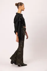 Pantalón de jean con estampado camuflado en tonos verdes y marrones, de corte oxford con bota ancha. Presenta bolsillos tipo cargo laterales, detalles de tachas metálicas en la cintura y bolsillos, y cierre frontal con botón.