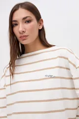 Remera de manga larga con diseño a rayas horizontales en color crema y rojo. Presenta un corte holgado, cuello redondo y un pequeño bordado en el pecho.