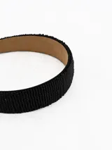 Vincha rígida de color negro, recubierta con pequeñas cuentas que le otorgan una textura granulada y un acabado brillante. El interior está forrado en material suave de color beige.