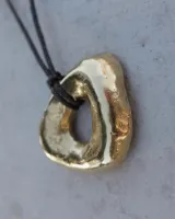 Collar con dije de forma irregular en tonos dorados y plateados, suspendido de un cordón doble de algodón negro.