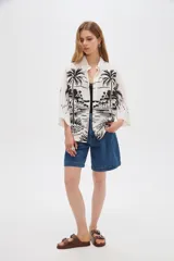 Camisa de viscosa de corte holgado, color blanco con estampado negro de paisaje con palmeras, cuello camisero y cierre frontal con botones.