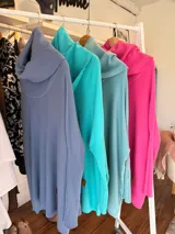 Polerón oversize de tejido de punto en color fucsia, con cuello alto tipo polera, mangas largas con puños acanalados y diseño holgado. Presenta un aplique decorativo en cuero en la parte inferior.