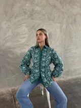 Camisa de manga larga con diseño de flores bordadas en color blanco sobre fondo verde. Presenta cuello clásico, cierre frontal con botones y mangas abullonadas con puños elásticos.