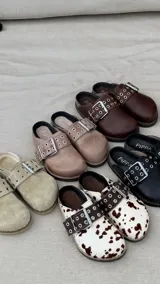 Zueco de cuero color beige, con hebilla metálica y remaches.