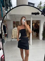 Pollera corta de cuero sintético con diseño de paneles y bolsillos frontales grandes. Presenta un corte recto y tiro medio.