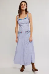 Vestido largo con diseño a rayas celestes y blancas, tirantes anchos, escote cuadrado y bolsillos frontales. Cuenta con delicados detalles de bordado floral multicolor en el pecho, tirantes y bolsillos.