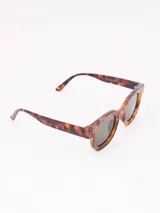 Lentes de sol con armazón grueso de acetato color beige claro, forma ovalada y lentes con degradado marrón.