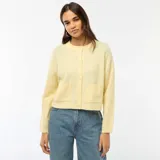 Cardigan de punto color amarillo suave, con cuello redondo, cierre frontal de botones y dos bolsillos de parche delanteros. Presenta mangas largas con puños acanalados y un corte recto.