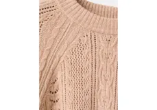 Jersey de punto trenzado color beige, con cuello redondo, manga larga y detalles de calados en el frente y las mangas.