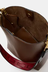 Bolso de hombro tipo saca en color marrón, con diseño minimalista y cierre de clip metálico. Incluye una correa de hombro con detalles troquelados en contraste y herrajes dorados.