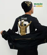 Remera de algodón color negro con cuello redondo y mangas cortas. Presenta una estampa de gran tamaño en la espalda que ilustra a Ronaldinho con un balón sobre la cabeza y el número 10, acompañada por el texto 'O Mago da Bola'.