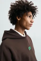 Sudadera con capucha de corte relajado, color marrón oscuro, con interior perchado. Presenta un bolsillo frontal tipo canguro, bordado con la palabra 'LOVE' en el pecho y un parche decorativo a contraste en el bolsillo. Posee puños y ruedo en rib.