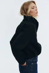 Campera negra de tejido efecto neopreno, con cuello chimenea alto, cierre frontal metálico y bajo fruncido con elástico. Presenta hombros caídos y corte corto.