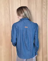 Camisa de manga larga con estampado de cuadros en tonos marrones y azules. Presenta cuello alto con volados, cierre frontal con botones y puños con volados.