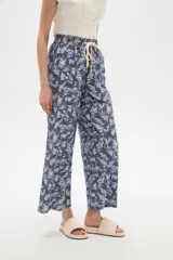 Pantalón de algodón estampado con diseño botánico de hojas en tonos verdes sobre base blanca, de corte holgado, tiro medio y cintura elástica con cordón de ajuste ajustable.