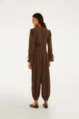 Pantalón babucha marrón de corte amplio y holgado, con cintura alta elastizada y cordón ajustable. Cuenta con puños fruncidos con elástico en los tobillos y está confeccionado en mezcla de viscosa y poliamida con forro de viscosa.