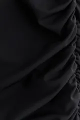 Vestido corto entallado de punto elástico, con diseño asimétrico de un solo hombro y manga larga. Presenta una capa superior drapeada y costuras fruncidas laterales que crean un efecto de pliegues en toda la prenda.