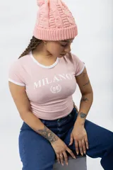Remera ajustada de manga corta color marrón oscuro, con cuello redondo y ribetes blancos en el cuello y mangas. Presenta un estampado frontal en blanco con el texto "MILANO" y un escudo con el número "96".