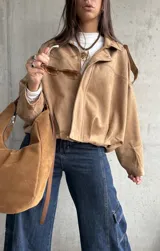 Campera tipo bomber de gamuza con diseño relajado, cierre frontal, cuello camisero y detalles de apliques en los hombros.
