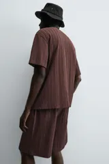 Bermuda de corte relajado color marrón oscuro, confeccionada en tejido jacquard con textura acanalada vertical. Presenta cintura elástica ajustable con cordón, bolsillos delanteros y un bolsillo trasero de plastrón.