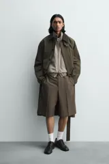 Bermuda de vestir color marrón oscuro, corte relajado y tiro alto, con pliegues frontales y cierre de botón y cremallera.