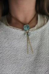 Collar artesanal con tiento marrón, dije de piedra turquesa irregular, perlas y colgantes de metal dorado.