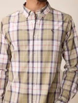 Camisa de manga larga con cuello abotonado y cierre frontal de botones. Presenta un diseño de cuadros en tonos beige, blanco y azul con líneas finas en rojo.
