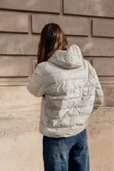 Campera puffer ultraliviana color beige, con diseño acolchado horizontal, capucha incorporada, cierre frontal y bolsillos laterales.