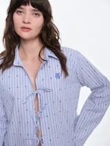 Camisa de dormir de popelina de algodón, con estampado de rayas verticales y pequeños motivos geométricos. Presenta cuello camisero, mangas largas y cierre frontal mediante lazos ajustables.