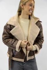 Campera oversize de efecto cuero color marrón con interior, solapas, cuello y puños de corderito sintético en tono tostado. Cuenta con detalles de tiras ajustables con hebilla en el cuello, mangas y ruedo, y cierre frontal cruzado.