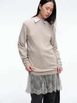 Sweater de tejido de punto color beige, con cuello redondo y mangas largas. Presenta un diseño de largo extendido con un delicado aplique de encaje en el ruedo inferior.
