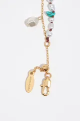 Pulsera de doble tira dorada combinada con cuentas de perlas y dijes colgantes de piedras naturales de colores, resina y perla barroca. Incorpora cierre de mosquetón con cadena de alargue.