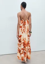 Vestido largo de corte recto y tejido fluido, con estampado de palmeras en tonos naranjas sobre fondo crema. Presenta cuello halter con detalle fruncido, tirantes finos ajustables y cierre de lazo en la espalda.