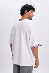 Remera manga corta blanca de corte holgado, con cuello redondo y puños acanalados en tono bordó con líneas blancas. Cuenta con un pequeño bordado circular en el pecho con la inscripción "NYC Well-Being Association" y un diseño de red.