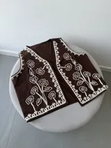 Chaleco marrón con bordados florales en color crema en los bordes y el frente. Presenta un diseño sin mangas con escote en V.