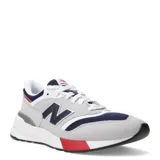 Championes urbanos New Balance modelo 997R, con diseño inspirado en el running de los años 90. Presentan una combinación de colores gris, azul marino, blanco y detalles en rojo. Confeccionados con paneles de gamuza y malla textil, cuentan con el logo N en los laterales y suela con tecnología de amortiguación.