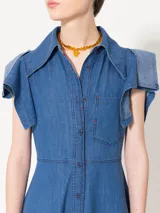 Vestido camisero midi de denim azul con silueta relajada. Tiene mangas cortas rebatidas, recorte a contratono en la falda y acceso frontal con botones.