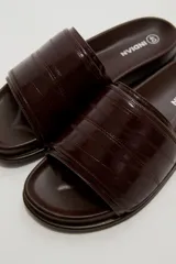Sandalias planas color marfil, con tira ancha acolchada en el empeine y suela baja con borde oscuro.