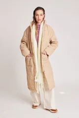 Campera larga acolchada color beige, con diseño de costuras onduladas, cuello alto, cierre frontal con botones a presión y bolsillos laterales amplios.