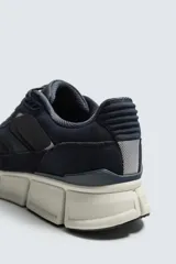 Zapatilla deportiva azul marino con detalles en gris oscuro y blanco. La parte superior está fabricada en combinación de piel con acabado serraje y tejido técnico transpirable. Cuenta con una suela ligera y voluminosa.
